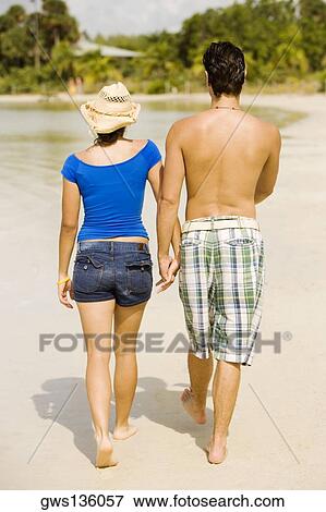 Stock Photo - Rear view of a young man and a teenage girl walking on the beach. Fotosearch