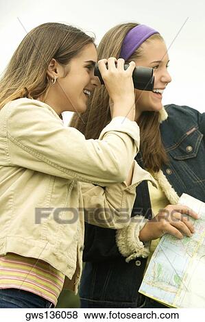 Stock Photo - Side profile of a girl looking through a par of binoculars with a girl holding a map. Fotosearch