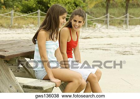 Side profile of two teenage girls sitting on a wooden bench on the beach View Large Photo Image Stock Photo - Side profile of two teenage girls sitting on a wooden bench on the beach. Fotosearch