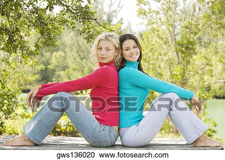 Stock Image - Side profile of two young women sitting back to back. Fotosearch