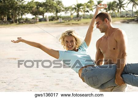 Young man carrying a young woman on the beach View Large Photo Image Stock Photo - Young man carrying a young woman on the beach. Fotosearch