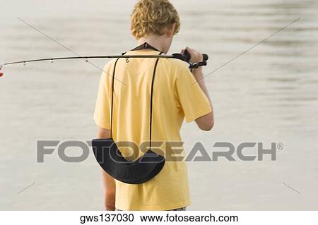 Stock Image - Rear view of a teenage boy holding a fishing rod. Fotosearch