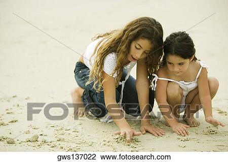 Two sisters playing with sand on the beach View Large Photo Image Stock Image - Two sisters playing with sand on the beach. Fotosearch