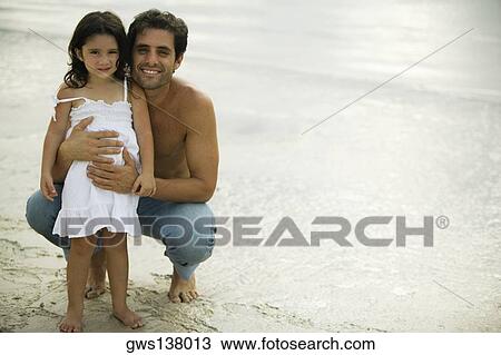 Stock Image - Portrait of a father holding his daughter on the beach. Fotosearch