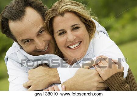 Stock Image - Portrait of a mature man embracing a mid adult woman from behind. Fotosearch