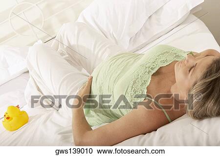 Stock Image - High angle view of a pregnant woman resting on the bed. Fotosearch