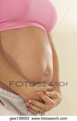 Stock Image - Mid section view of a pregnant woman touching her abdomen. Fotosearch