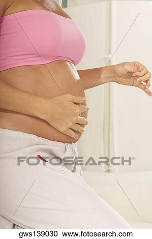 Mid section view of a pregnant woman touching her abdomen View Large Photo Image Stock Image - Mid section view of a pregnant woman touching her abdomen. Fotosearch