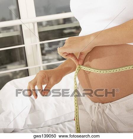 Mid section view of a pregnant woman measuring her abdomen with a measuring tape View Large Photo Image Stock Image - Mid section view of a pregnant woman measuring her abdomen with a measuring tape. Fotosearch