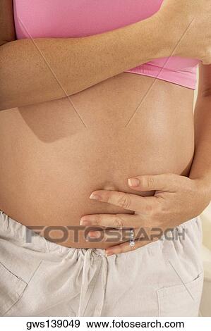 Stock Photo - Mid section view of a pregnant woman touching her abdomen. Fotosearch
