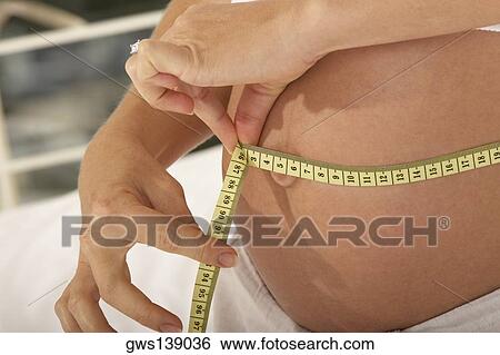 Mid section view of a pregnant woman measuring her abdomen with a measuring tape View Large Photo Image Stock Photograph - Mid section view of a pregnant woman measuring her abdomen with a measuring tape. Fotosearch