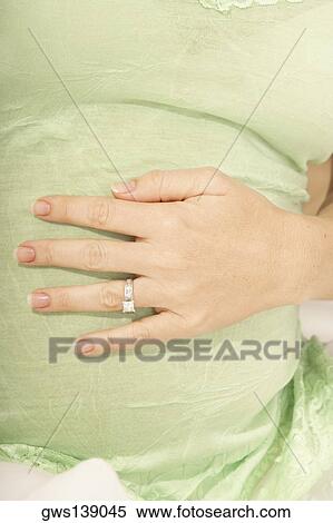 Stock Photography - Mid section view of a pregnant woman touching her abdomen. Fotosearch