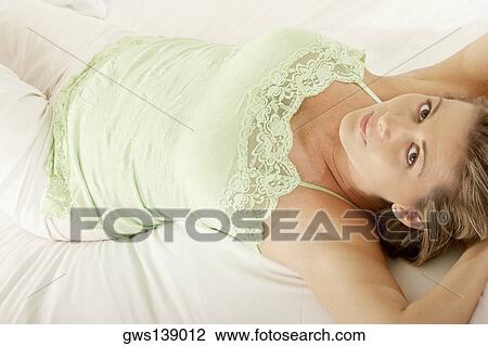 Stock Image - Portrait of a mid adult woman lying on the bed. Fotosearch