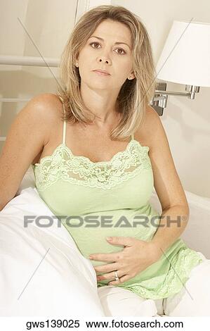 Stock Photography - Portrait of a mid adult woman touching her stomach. Fotosearch