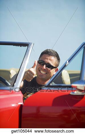 Close-up of a young man sitting in a car showing a thumbs up sign View Large Photo Image Picture - Close-up of a young man sitting in a car showing a thumbs up sign. Fotosearch