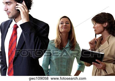 Stock Photo - Businessman talking on a mobile phone with his two secretaries standing behind him. Fotosearch
