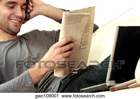 Young man reading a newspaper and talking on a mobile phone View Large Photo Image Stock Image - Young man reading a newspaper and talking on a mobile phone. Fotosearch