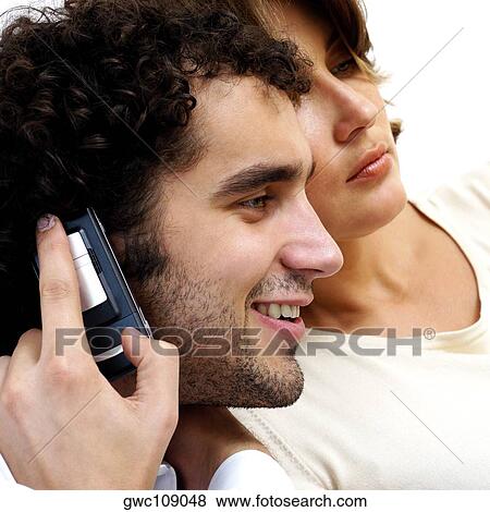 Stock Photo - Young man talking on a mobile phone with a young woman beside him. Fotosearch