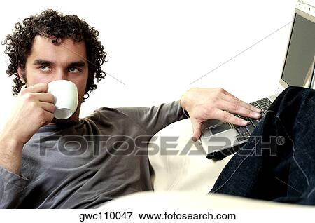 Young man drinking a cup of tea using a laptop View Large Photo Image Stock Photo - Young man drinking a cup of tea using a laptop. Fotosearch