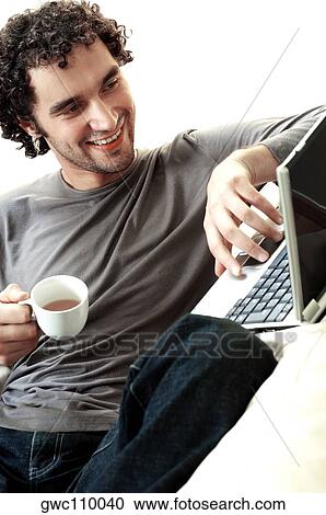Young man holding a cup of tea using a laptop View Large Photo Image Stock Image - Young man holding a cup of tea using a laptop. Fotosearch