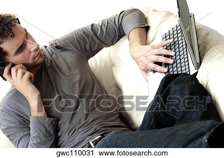 Young man talking on a mobile phone and using a laptop View Large Photo Image Stock Image - Young man talking on a mobile phone and using a laptop. Fotosearch