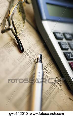 Stock Image - Close-up of a fountain pen with a calculator and eyeglasses on a financial page. Fotosearch