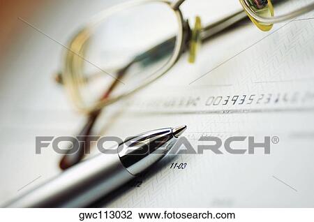 Stock Image - Close-up of a pen and eyeglasses on a check. Fotosearch