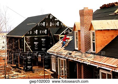 Stock Image - Man putting roof on new home. Fotosearch