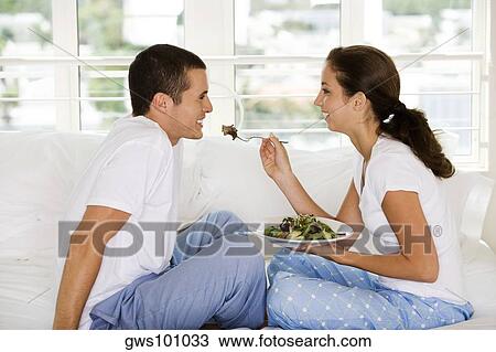Stock Image - Side profile of a young woman feeding a young man salad. Fotosearch