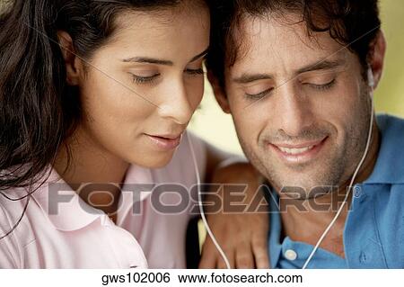 Stock Photograph - Close-up of a mid adult man and a young woman listening to music through headphones. Fotosearch