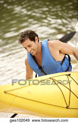 Stock Photo - High angle view of a mid adult man carrying a kayak and an oar. Fotosearch