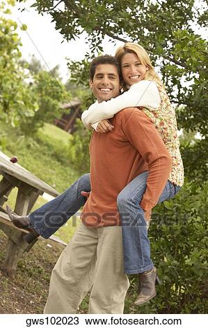 Stock Image - Side profile of a young woman riding piggyback on a mid adult man. Fotosearch