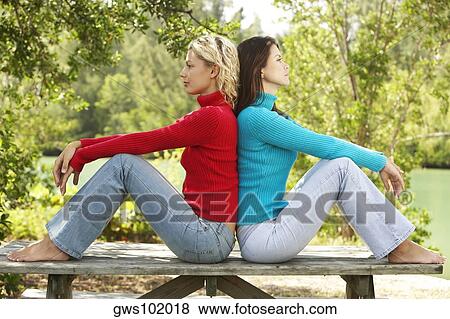 Side profile of two young women sitting back to back View Large Photo Image Stock Photo - Side profile of two young women sitting back to back. Fotosearch