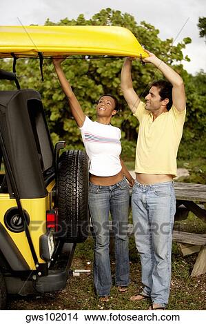 Young woman and a mid adult man loading a kayak on a jeep View Large Photo Image Picture - Young woman and a mid adult man loading a kayak on a jeep. Fotosearch