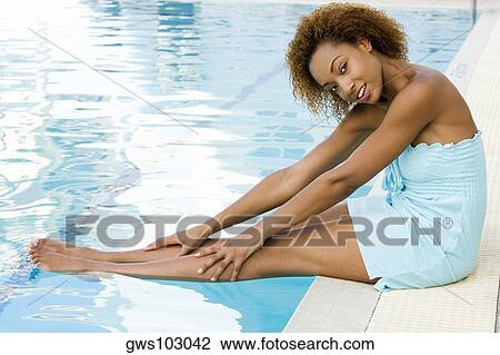 Stock Image - Portrait of a young woman sitting at the edge of a swimming pool. Fotosearch