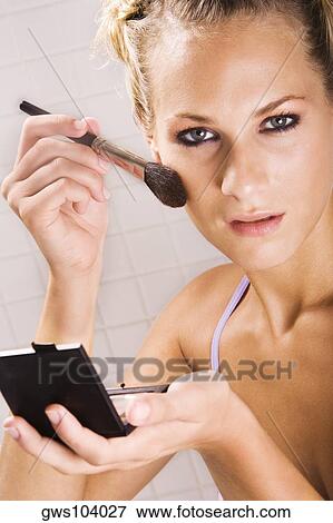 Stock Photo - Portrait of a young woman applying blush with a brush. Fotosearch