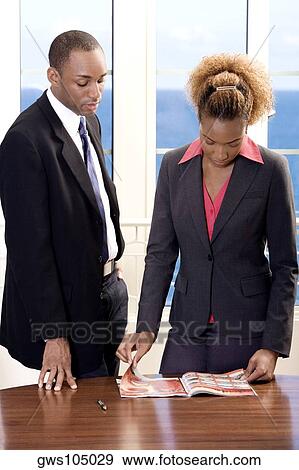 Stock Photo - Businessman and a businesswoman reading a magazine in an office. Fotosearch