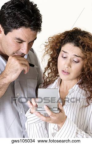 Picture - Close-up of a young woman and a mid adult man using a calculator. Fotosearch
