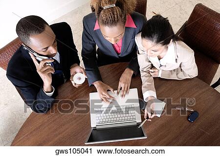High angle view of two businesswomen using a laptop with a businessman talking on a mobile phone View Large Photo Image Stock Image - High angle view of two businesswomen using a laptop with a businessman talking on a mobile phone. Fotosearch
