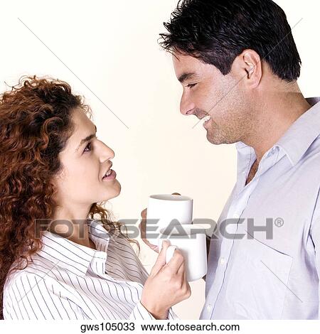 Stock Image - Side profile of a young woman and a mid adult man holding coffee cups. Fotosearch