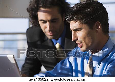 Stock Image - Two businessmen working on a laptop. Fotosearch