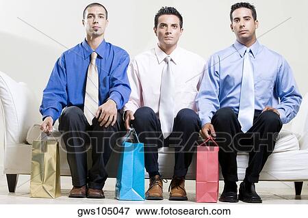Two young men and a mid adult man sitting on a couch holding shopping bags View Large Photo Image Stock Photo - Two young men and a mid adult man sitting on a couch holding shopping bags. Fotosearch