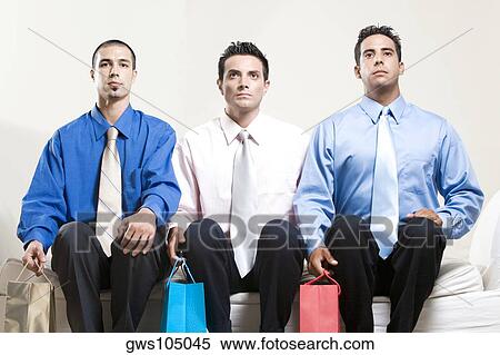 Two young men and a mid adult man sitting on a couch holding shopping bags View Large Photo Image Stock Photography - Two young men and a mid adult man sitting on a couch holding shopping bags. Fotosearch