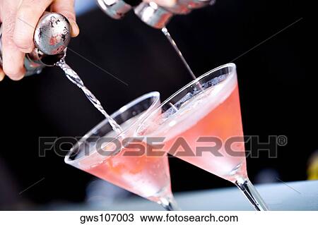 Stock Image - Close-up of a person's hand pouring martini into martini glasses. Fotosearch
