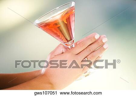 Stock Image - Close-up of a woman's hand holding a glass of martini. Fotosearch