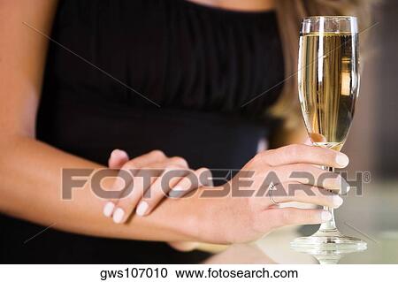 Mid section view of a young woman holding a champagne flute View Large Photo Image Stock Image - Mid section view of a young woman holding a champagne flute. Fotosearch