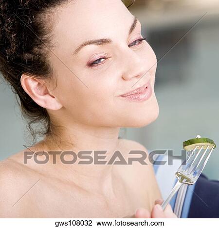 Stock Image - Close-up of a young woman eating a cucumber slice with a fork. Fotosearch
