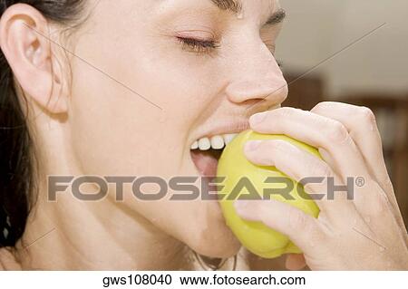 Stock Image - Close-up of a young woman eating a green apple. Fotosearch