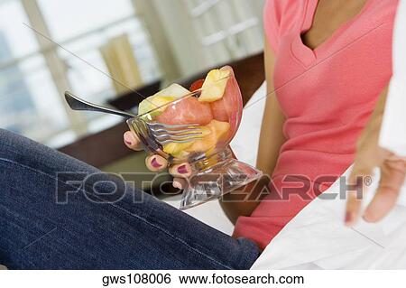Stock Photograph - Mid section view of a young woman holding a bowl of fruit salad. Fotosearch