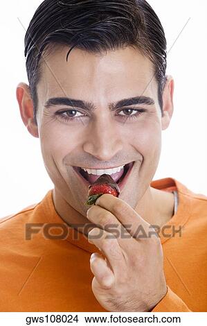 Picture - Portrait of a mid adult man eating a chocolate dipped strawberry. Fotosearch